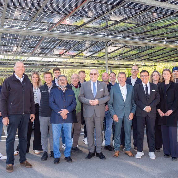 Einweihnung Parkplatz-PV-Anlage Gruppe von Mitarbeitenden und Projektbeteiligten steht unter einer überdachten Parkplatzanlage mit installierten Photovoltaikmodulen