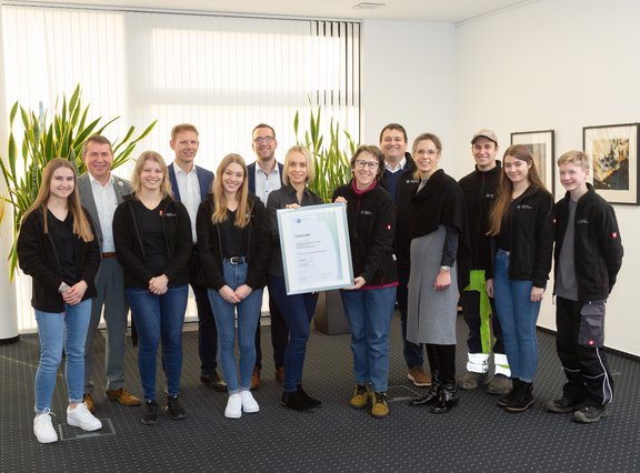 Auszubildende halten einen großen Bilderrahmen mit Urkunde