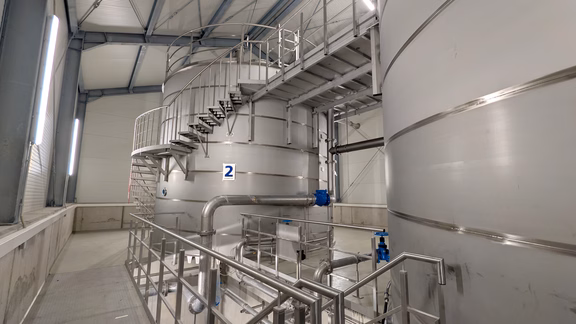 Blick in das Innere des neuen Hochbehälters Stuppach. Zu sehen sind mehrere Edelstahlbehälter, Rohrleitungen, Treppenanlagen und technische Einrichtungen zur Speicherung und Verteilung von Trinkwasser.