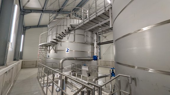 Blick in das Innere des neuen Hochbehälters Stuppach. Zu sehen sind mehrere Edelstahlbehälter, Rohrleitungen, Treppenanlagen und technische Einrichtungen zur Speicherung und Verteilung von Trinkwasser.