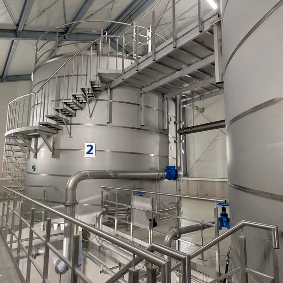 Blick in das Innere des neuen Hochbehälters Stuppach. Zu sehen sind mehrere Edelstahlbehälter, Rohrleitungen, Treppenanlagen und technische Einrichtungen zur Speicherung und Verteilung von Trinkwasser.