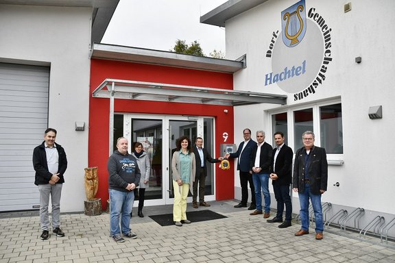 Verantworliche stehen vor rot-weißem Gebäude mit Defibrillator