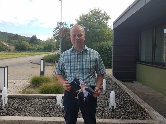 Man steht vor Brunnen und hält seinen Gewinn einen eingepackten Gutschein in den Händen