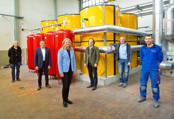 Verantwortliche sehen im Heizgebäude vor großen gelben und etwas kleineren roten Gastanks
