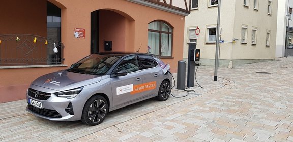 Grauer Opel E-Corsa steht an Ladesäule vor braunem Gebäude