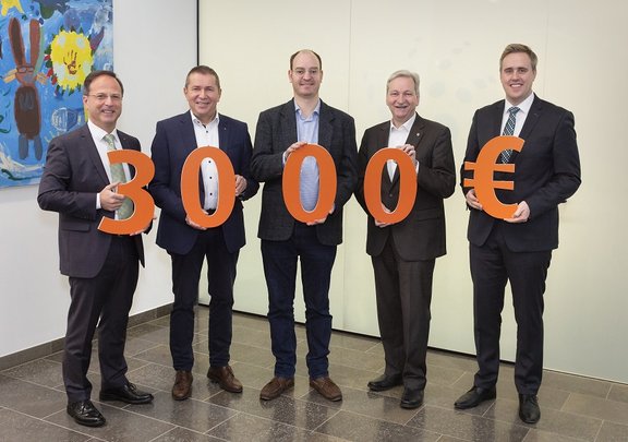 Geschäftsführung und Bürgermeister stehen nebeneinander und halten in großen orangenen Buchstaben 3.000