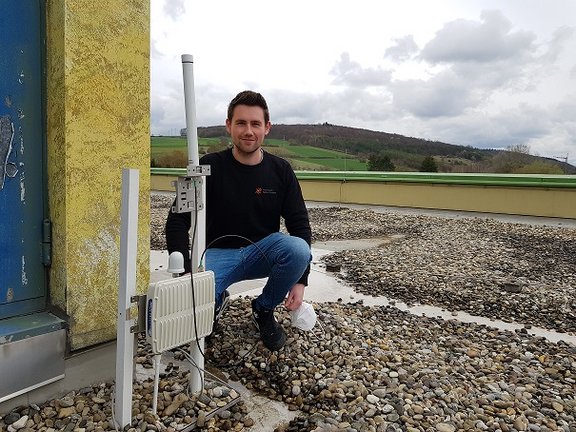 Mitarbeiter im schwarzen Pulli kniet nehmen LoRaWAN Funksensor auf Gebäudedach