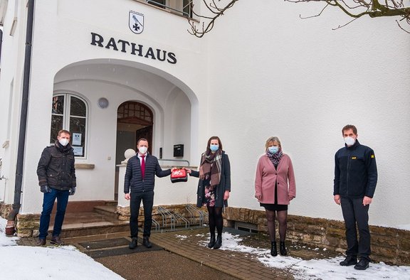 Verantwortliche stehen vor weißem Gebäude und ein Defibrilltor wird übergeben.