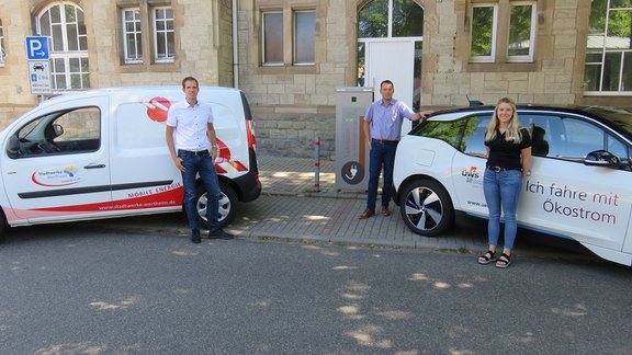 2 Elektroautos stehen an einer Ladesäule und die Firmenvertreter davor