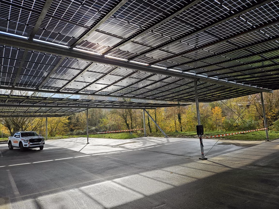 Ein Auto steht auf einer Parkplatzfläche, die mit PV-Modulen überdacht ist. Die Sonne scheint durch die Paneele und es ist ein freundlicher Wintertag.