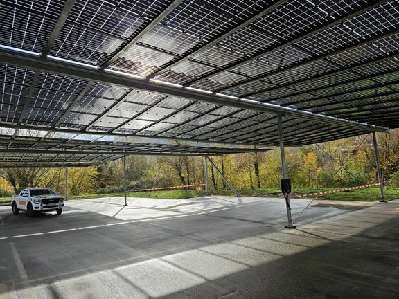 Ein Auto steht auf einer Parkplatzfläche, die mit PV-Modulen überdacht ist. Die Sonne scheint durch die Paneele und es ist ein freundlicher Wintertag.