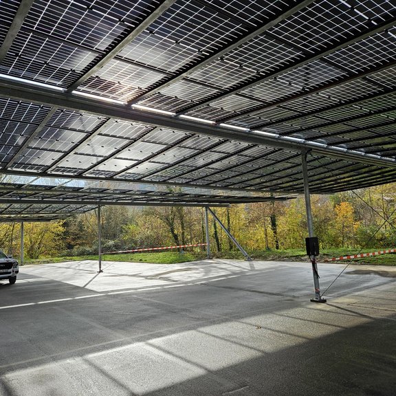 Ein Auto steht auf einer Parkplatzfläche, die mit PV-Modulen überdacht ist. Die Sonne scheint durch die Paneele und es ist ein freundlicher Wintertag.