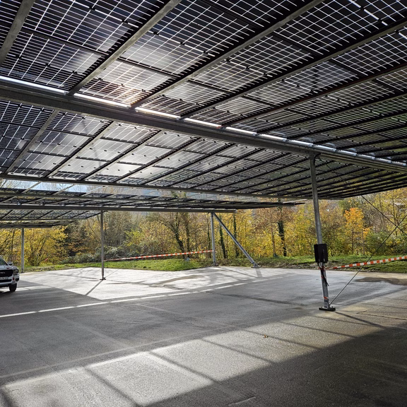 Parkplatz-PV-Anlage Ein Auto steht auf einer Parkplatzfläche, die mit PV-Modulen überdacht ist. Die Sonne scheint durch die Paneele und es ist ein freundlicher Wintertag.