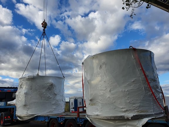 Zwei große runde Betonbehälter, eingepackt in weißer Folie am Kran