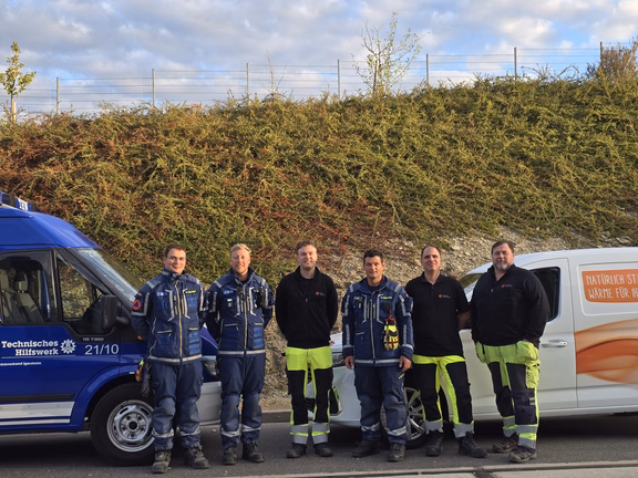 THW Drohnenübung Sechs Personen in Einsatz- und Arbeitskleidung vor einem THW-Fahrzeug und einem weißen Firmenfahrzeug.