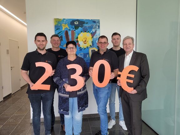 Mitarbeiter stehen in einer Gruppe zusammen und halten in großen orangenen Buchstaben 230