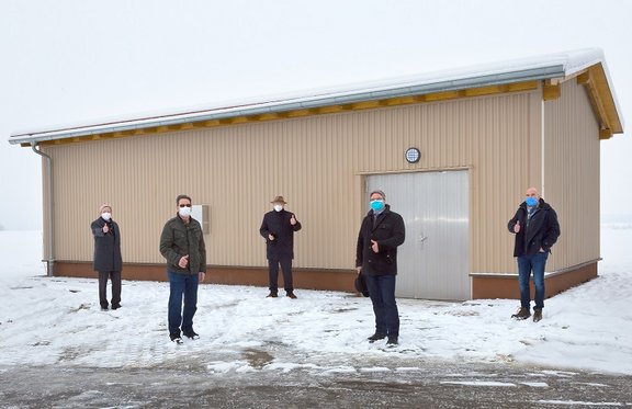 Verantwortliche stehen im Schnee vor einem hellbraunen Gebäude