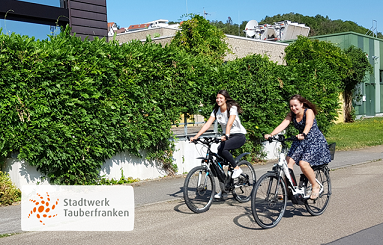 2 Frauen fahren nebeneinander im Sommer auf einem Fahrrad