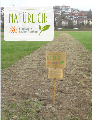 umgegrabene Ackerfläche mit einem Holzschild "Blühwiese" im Vordergrund