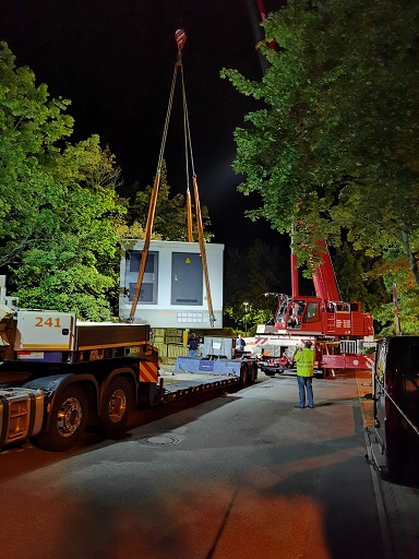 Roter Autokran hebt eine weiße Trafostation von einem Tieflader herunter