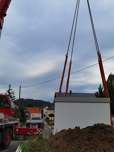 Weiße Trafostation hängt an Seilen von einem Autokran