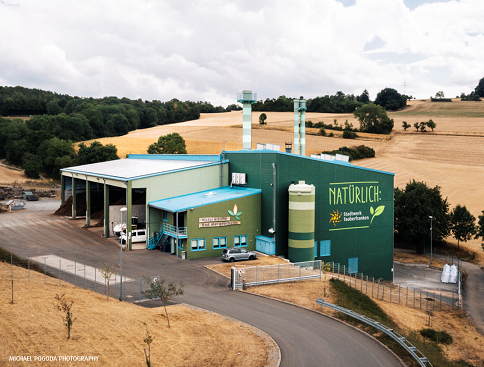 Naturwärmekraftwerk Blick auf das grüne Naturwärmkraftwerk mit Kaminen umgeben von Feldern im Sommer