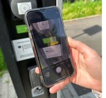 Ad hoc laden Hand hält ein Smartphone vor eine Ladestation, auf dem Bildschirm ist eine QR-Code-Scan-App geöffnet.