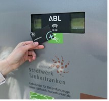 Ladekarte Eine Hand hält eine Ladekarte an ein Kartenlesegerät an einer E-Ladesäule mit der Aufschrift „ABL“ und dem Logo des Stadtwerks Tauberfranken.